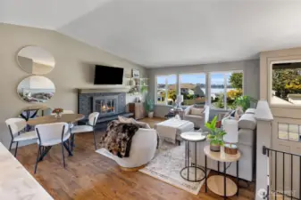 Living room with vaulted ceiling, hardwood floors, wood burning fireplace and wall of windows providing breathtaking views of Lake Stevens