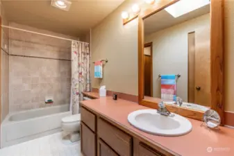 Continental hall full bath with pocket door access to Primary Bedroom.  Single vanity.  Tub/Shower with tile surround.  Large linen closet.  Skylight.