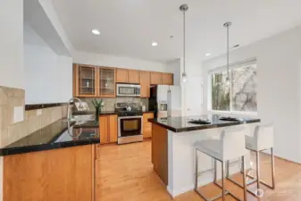This inviting kitchen features warm wood cabinetry, sleek stainless-steel appliances, and rich granite countertops that offer both style and durability. A spacious center island with bar seating anchors the room, illuminated by modern pendant lighting for an elevated touch. The open layout flows seamlessly into the dining area, enhanced by natural light from the nearby window and complemented by clean, contemporary finishes throughout. It’s a functional and welcoming space designed for everyday living and effortless entertaining.
