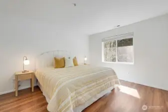 Calming primary suite offers a bright and restful retreat with soft natural light and a clean, modern aesthetic. The large window frames peaceful views of the private, tree-lined backyard, creating a sense of tranquility from the moment you step inside. Warm wood flooring, a neutral palette, and thoughtful finishes make this an inviting space to unwind and recharge.