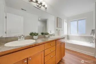 The primary suite is complemented by a bright and beautifully designed ensuite featuring a double-sink vanity, modern lighting, and warm wood-tone flooring. A soaking tub sits beneath a frosted window that brings in soft natural light while maintaining privacy, creating a spa-like feel. Clean lines, contemporary finishes, and a thoughtful layout make this an inviting extension of the primary retreat.