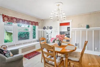 The formal room is flooded with charm and natural light, showcasing large picture windows and a built-in bench. Adjacent to main level hallway and an updated kitchen.