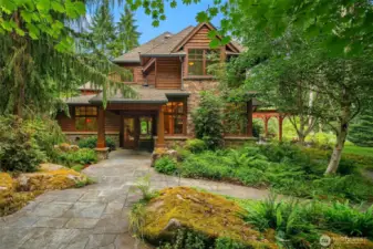 View of the home from the south showcasing the massive rocks “planted” by the landscaper and the stone walkways lining the lush greenery.