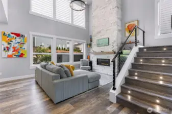 Large living room with vaulted ceilings, stone fireplace, and a wall of windows with custom blinds.