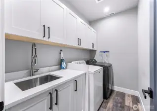 Upstairs laundry room with utility sink and quartz counters.
