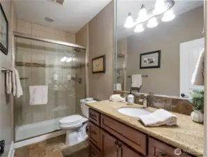 Hall bath with travertine tile floors, single vanity with granite countertop and shower with tile surround.
