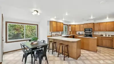 This expansive kitchen offers abundant cabinetry, generous counter space, and a large peninsula with bar seating—ideal for casual meals or entertaining. The open layout flows into a charming dining nook, highlighted by a large picture window that frames lush greenery
