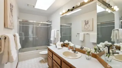 This bright and cheerful full bath features a skylight, a spacious vanity with great storage, and a tub/shower combo with glass doors—perfect for daily use or welcoming guests