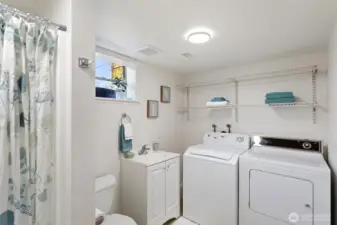 Updated lower-level ¾ bath with integrated laundry, featuring a refreshed vanity, LVP flooring, updated lighting, and natural light from a window. Clean and functional, with washer and dryer included.