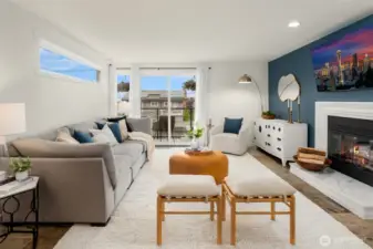 The spacious living room is anchored by a wood-burning fireplace with a natural stone  hearth and custom built-ins, creating a cozy, inviting space. Large windows flood the room  with light and frame partial views of Elliott Bay, the Seattle skyline, and the Space Needle.