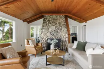 Warm and inviting living room with a stunning river rock fireplace, wood-paneled ceiling, and sound views—cozy island charm at its finest.