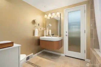 A privacy-diffused glass door opens from the primary bath to the back/side patio with planting beds, and welcomes soft light into the room.