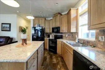 Step into a kitchen that's both beautiful and functional. Featuring warm, natural wood cabinets and stunning speckled countertops, this space offers a large island with seating, perfect for casual meals or entertaining guests. Modern black appliances and a stylish tile backsplash complete the look, making it a true centerpiece of the home. This kitchen is a must-see for anyone who loves to cook and gather.