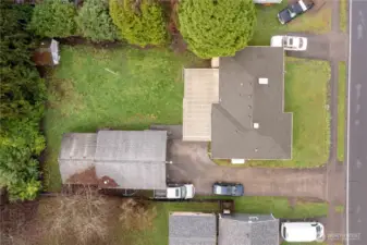 Aerial view shows the unpaved circular driveway area between the North & South driveways of home stretching between the covered patio & garage.