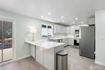 Beautiful, like new kitchen with light toned upper and lower cabinets, white countertops and stainless appliances and small breakfast bar.
