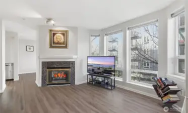 Living room with gas fireplace and floor to ceiling windows. Windows have remote control blinds. Updated LVP flooring.