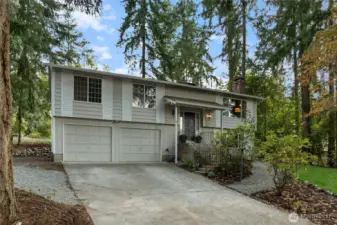 Updated home featuring two car garage, front lawn framed by evergreens.