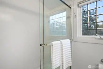 The upstairs full bathroom has marble tile flooring, a tub with tempered glass doors, a new toilet and a beveled glass double-pane window overlooking the gardens.