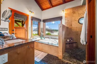 Primary bathroom features pebbled floors, jetted tub overlooking the amazing views, a shower with a port hole to gaze out and double sinks.