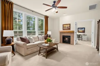 In the main living room, the large bright windows fill the room with natural light. The living space is anchored by a dual-sided fireplace that leads into the main floor office (or bonus room? playroom? Gym?)