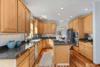 The kitchen boasts a center island with a gas stovetop & electric recessed over fan, tall classic wood cabinetry offering ample storage, and elegant granite countertops.