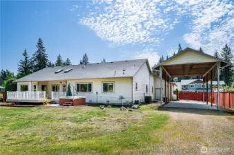 Rear view of the home featuring spacious covered RV parking. The propane tank in the distance is owned (not leased) and conveys with the property!