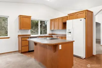 The kitchen is centered around the island, where the brand new glass top range sits right in the action, making cooking feel part of the conversation instead of tucked away. Seating on the opposite side keeps everyone close by, and the French door refrigerator with water and ice in the door handles the daily traffic easily. A large window over the sink looks out to a wooded backyard, giving you something nicer than a fence to stare at while doing dishes. The shaker style oak cabinetry is clean and simple, currently without hardware, which makes customizing the look refreshingly easy.