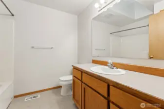 The main bathroom keeps things bright and functional with white walls, a long oak shaker vanity, and a wide landscape mirror that makes the space feel larger right away. Vinyl flooring handles daily traffic easily, and the full tub and shower combo keeps routines simple. The skylight is the quiet star here, pulling in natural light so mornings are just a bit brighter.