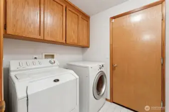 The laundry room keeps things straightforward and useful. The washer and dryer stay, including an LG front loading sensor dry dryer and a Maytag Neptune top loader that makes tossing in bulky items easy and saves you from bending down all the time. Vinyl flooring handles water and daily wear, and a full row of upper shaker oak cabinets matches the kitchen so storage doesn’t turn into a guessing game. There’s also a direct door to the two car garage, making this a natural drop zone for shoes, bags, and everything that follows you home.