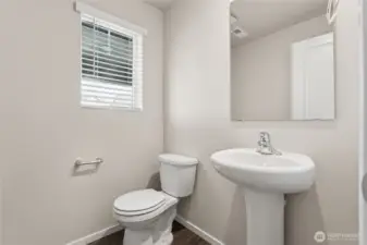 Convenient main-floor powder room featuring pedestal sink, toilet, mirror, window and luxury vinyl plank flooring. Photos are representative only and may display different color package and/or upgrades.