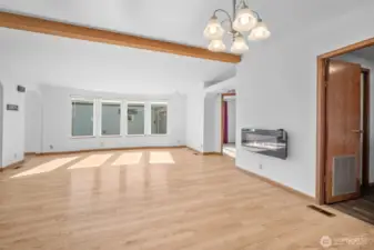 Open living area with hardwood floors, bright windows, and a cozy fireplace that conveys. Door on the right leads to the utility room.