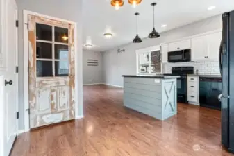 View looking toward living area and kitchen from dining room. White washed antique window pane door to panty compliments the wainscoting in dining area and custom designed island.