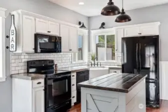 This kitchen offers cement counter tops, white subway tiles and cabinetry, farm style sink with new faucets, corner window, new lighting and highlights the dark wood counter top on island.