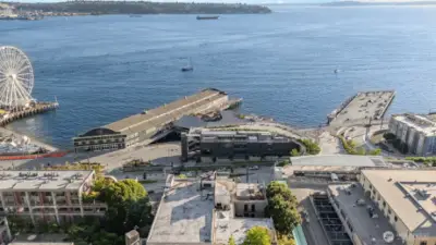 Capture the essence of Seattle waterfront living with this striking aerial view, featuring the shimmering Puget Sound, the iconic Great Wheel, and distant cargo ships dotting the horizon. The photo showcases the building's prime location near bustling piers and the Seattle Aquarium, with lush greenery and scenic water vistas enhancing the urban landscape. Enjoy unparalleled proximity to this vibrant waterfront hub, where every glance offers a picturesque blend of nature and city life!