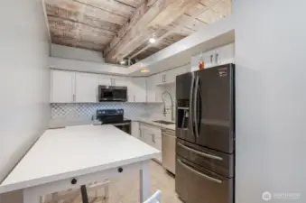 Whip up culinary delights in this modern kitchen, featuring sleek white cabinetry, a stylish mosaic tile backsplash, and a Samsung refrigerator. The photo highlights a spacious quartz countertop, stainless steel appliances including a double oven, and exposed wooden beams for a touch of historic charm.
