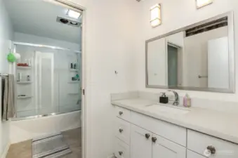 Refresh in this modern 1-bathroom, featuring a sleek quartz countertop and white cabinetry with ample storage. The photo showcases a spacious vanity with a large mirror, complemented by a glass-enclosed shower and tub combo, with stylish lighting and a clean design.