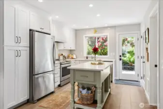 Open kitchen with island, stainless steel appliances, pantry storage and quartz countertops