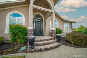 Elegant entry with arched windows, brick-accented steps, and double doors framed by classic pillars.