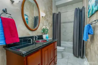 Stylish hall bath featuring a custom vessel sink, rich tile vanity with black accents, and full tub/shower with decorative tile detail—both functional and elegant.