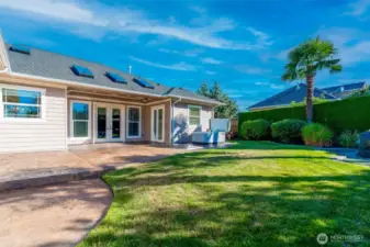 Private back yard with lush lawn, tropical landscaping, and stamped concrete patio leading to the hot tub—an inviting outdoor space for entertaining or relaxing.