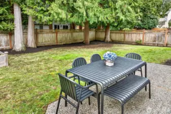 The fully fenced backyard pairs a patio for outdoor dining with a level lawn and a dramatic evergreen backdrop, creating a private setting for relaxing and entertaining in Amberley on English Hill.