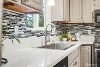 Stylish kitchen with stainless appliances, custom backsplash, and a view to the backyard.