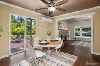 This dining space offers an open layout with direct sightlines to the living room and fireplace. Natural light from the glass doors brightens the room, highlighting the hardwood floors and creating an inviting spot for meals and gatherings.
