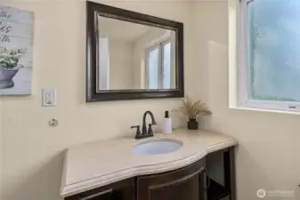 The main floor bathroom includes a spacious vanity, updated sink fixture, and framed mirror. Natural light flows in through the privacy window, brightening the space.