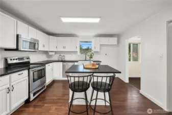 Bright and functional, this remodeled kitchen boasts crisp white cabinetry, black counters, and stainless steel appliances. The central island provides additional workspace and seating, making it ideal for cooking or casual dining.