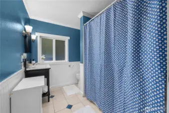The upstairs full bathroom combines modern updates with character, featuring crisp blue walls accented by classic white wainscoting. A full tub and shower with tile surround provide functionality, while natural light from the frosted window brightens the space.  This bathroom also offers direct access to the convenient laundry chute, making household routines easier by sending clothes straight down to the main-floor laundry area.