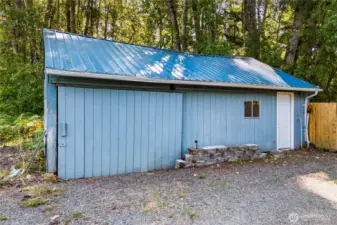 The detached garage offers excellent storage or workspace potential, set against a private treed backdrop for added seclusion. Its metal roof adds durability, making it a practical and lasting feature of the property.