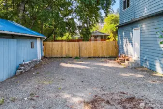 A spacious gravel parking area sits beside the garage, providing plenty of room for multiple vehicles, including RVs or trailers. Secure fencing adds privacy and defines the backyard space.