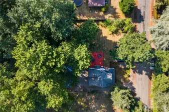 Bird’s-eye view directly above the property, showcasing the red deck, fenced backyard, and mature trees that provide privacy and shade. A clear look at the home’s layout and lot placement within the neighborhood.