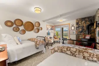 Relaxed guest bedroom 1 of two, ground level walkout daylight basement. Wood burning fireplace. Stone wall feature. Door to covered outdoor Patio and landscape mountain views.